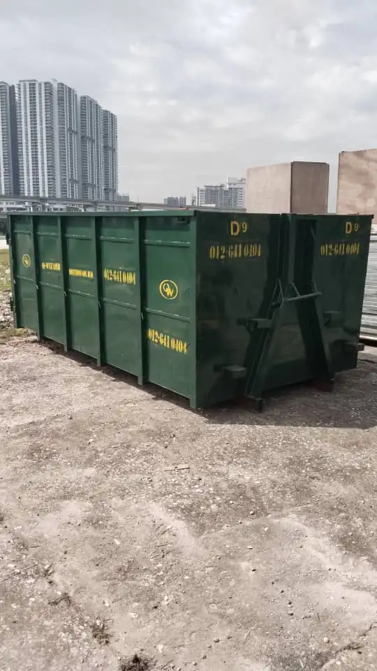 A line of empty green Q-Wizard RORO bins parked on hardstanding with the Kuala Lumpur skyline behind them.
