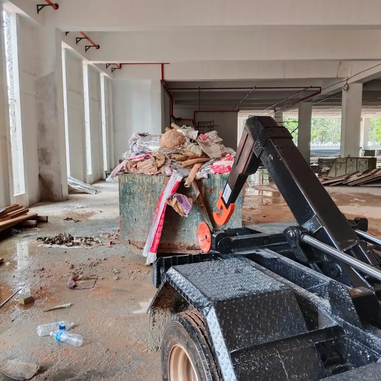 A RORO bin filled with cement bags, cardboard and packaging inside the concrete shell of a building under construction.