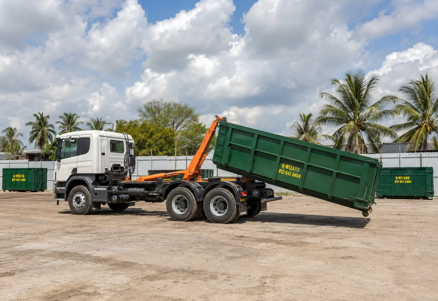 Illustrative hook-lift truck loading a green RORO bin in a Malaysian yard.
